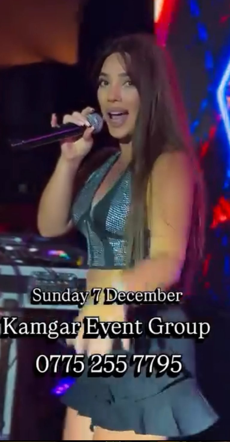 Female singer performing on stage with microphone wearing sparkly gray top with colorful stage lighting